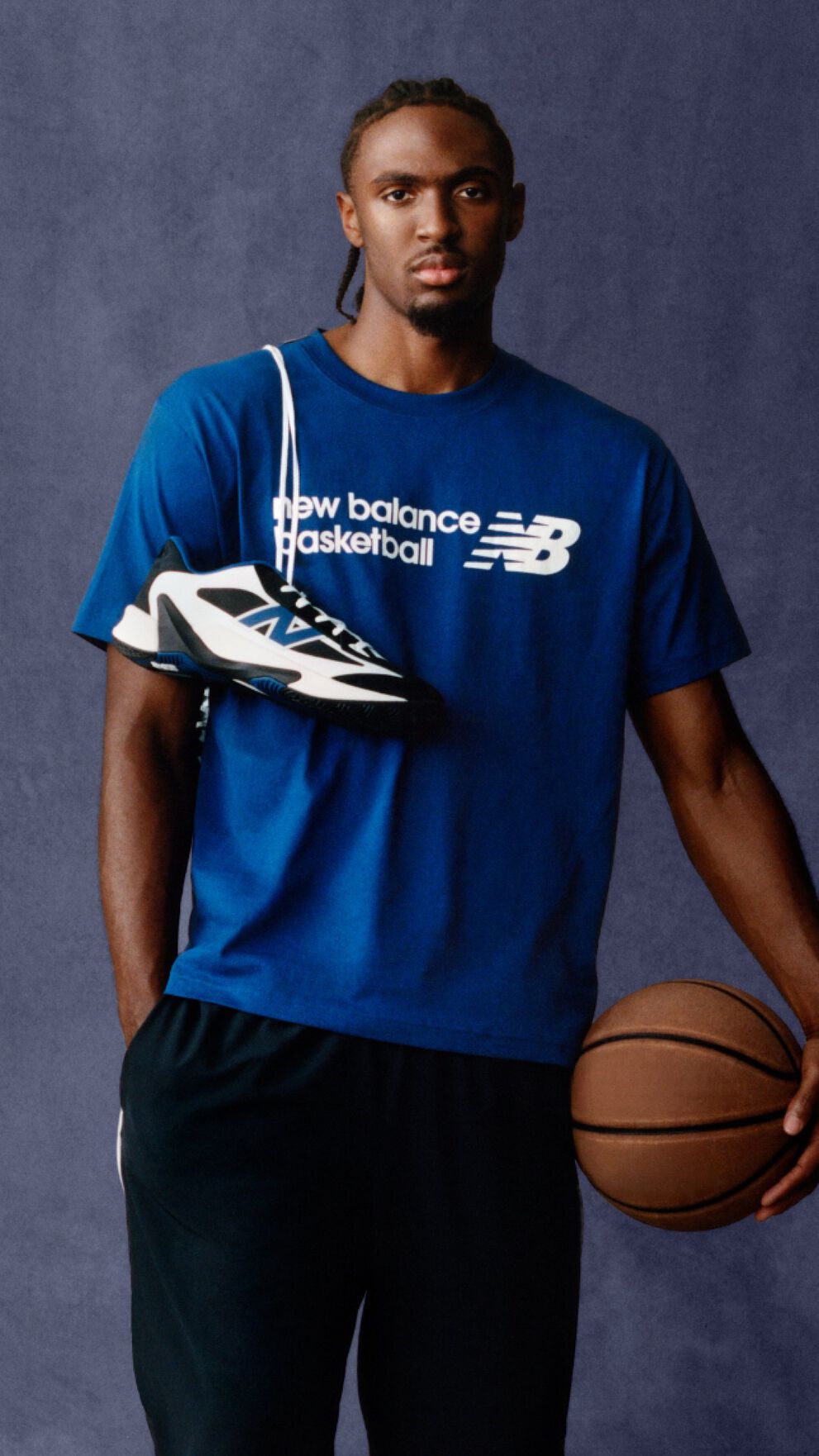 A person wearing a blue New Balance Basketball T‑shirt poses against a plain backdrop. 